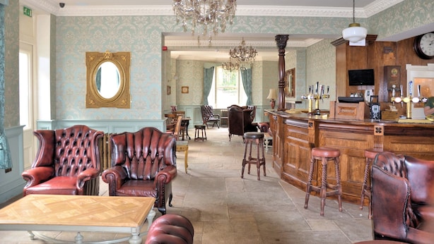 A bar area with leather chairs, a wooden bar counter, and a chandelier. - The Aston Tavern (Birmingham)