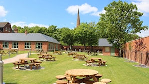 A courtyard with multiple picnic tables and a church steeple in the background. - The Aston Tavern (Birmingham)