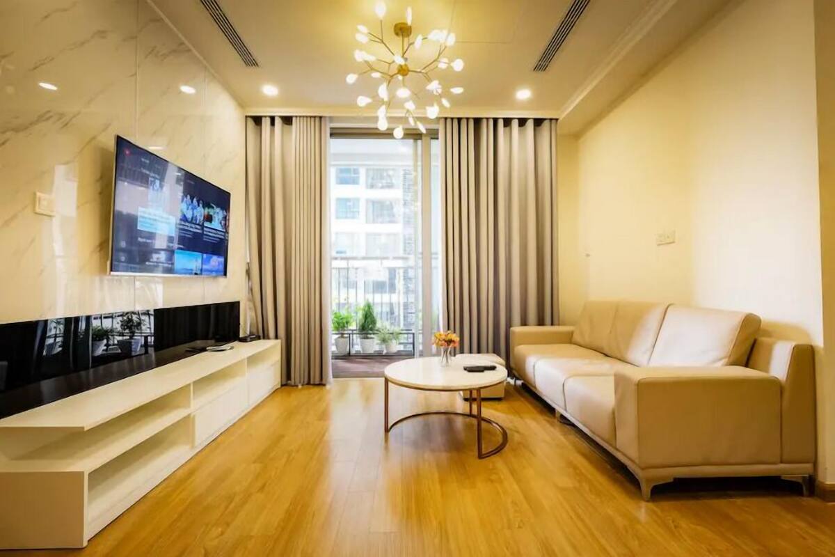 A modern living room with a flat-screen TV, a sofa, a coffee table, and a large window with curtains.