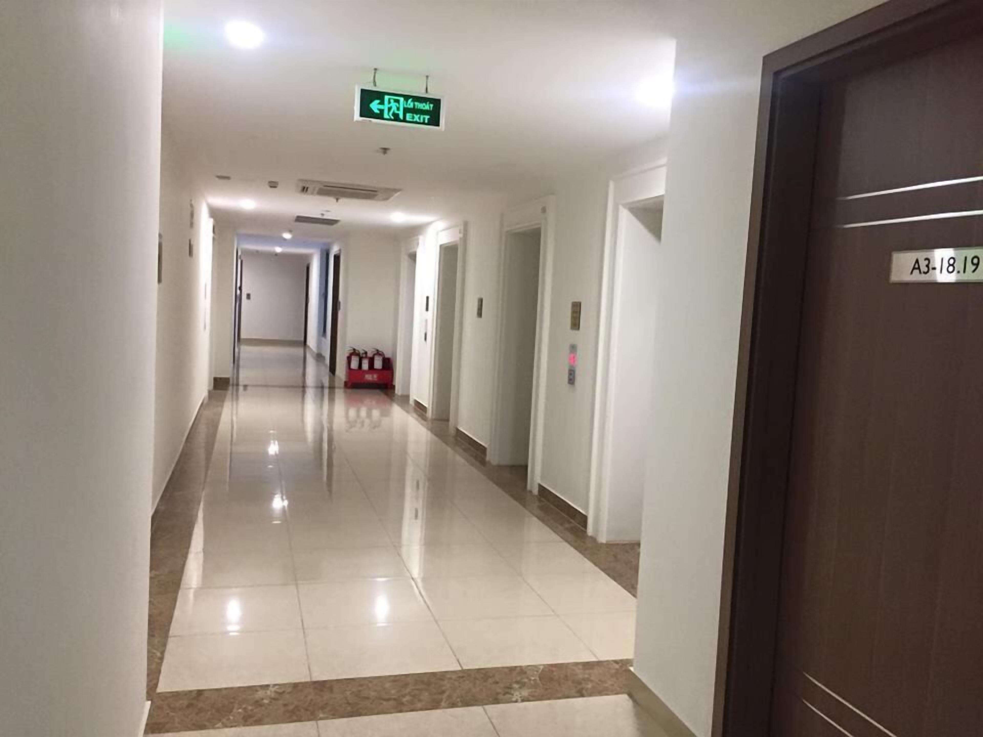 A long, well-lit hallway with a green exit sign, a fire extinguisher, and an elevator.
