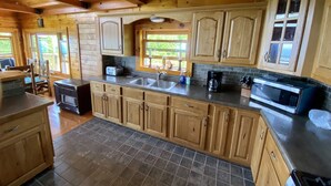 Cuina d'una cabana de fusta amb una illa gran, un forn integrat i una finestra amb vistes a vegetació.