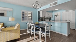 A modern kitchen with white cabinets, a central island, and a dining area with a table and chairs. - Bring Your Family to Our Gorgeous Oceanfront Condo (Myrtle Beach)