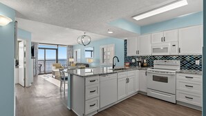 A modern kitchen with white cabinets, a large island, and a view to the outside. - Bring Your Family to Our Gorgeous Oceanfront Condo (Myrtle Beach)