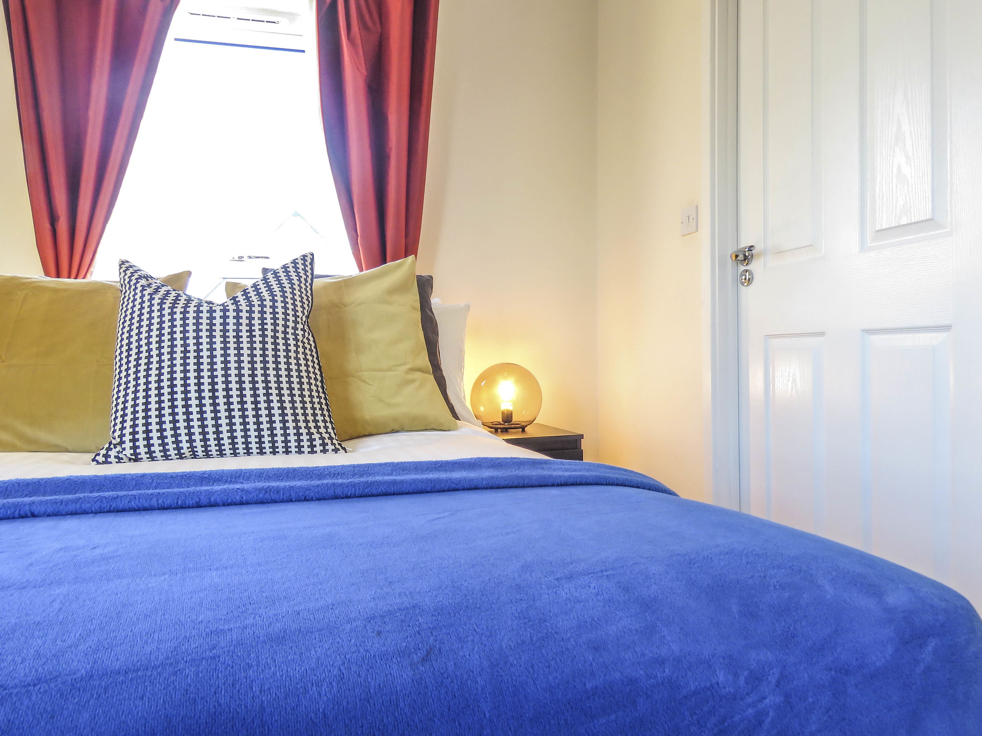 Un letto con una coperta blu, due cuscini, una lampada da comodino e una porta bianca.