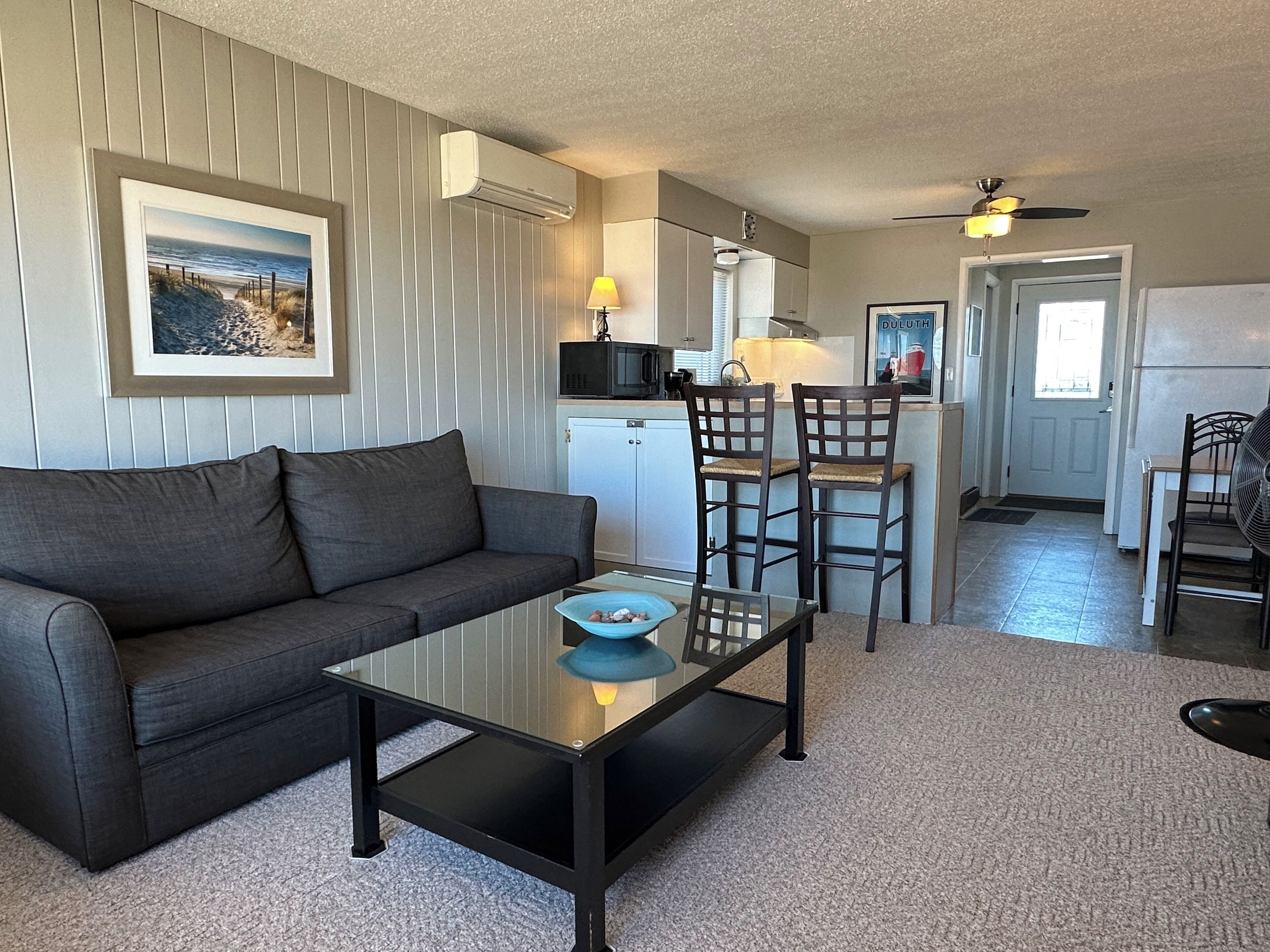 A living room with a sofa, a glass coffee table, and a kitchen area with a dining table and chairs.