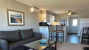 A living room with a sofa, a glass coffee table, and a kitchen area with a dining table and chairs. - Beachfront Getaway on Park Point - Easy Walking Distance to Canal Park (Duluth)