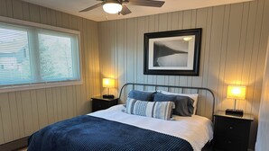 A bedroom with a bed, two bedside tables, a ceiling fan, a window with blinds, and a framed picture on the wall. - Beachfront Getaway on Park Point - Easy Walking Distance to Canal Park (Duluth)