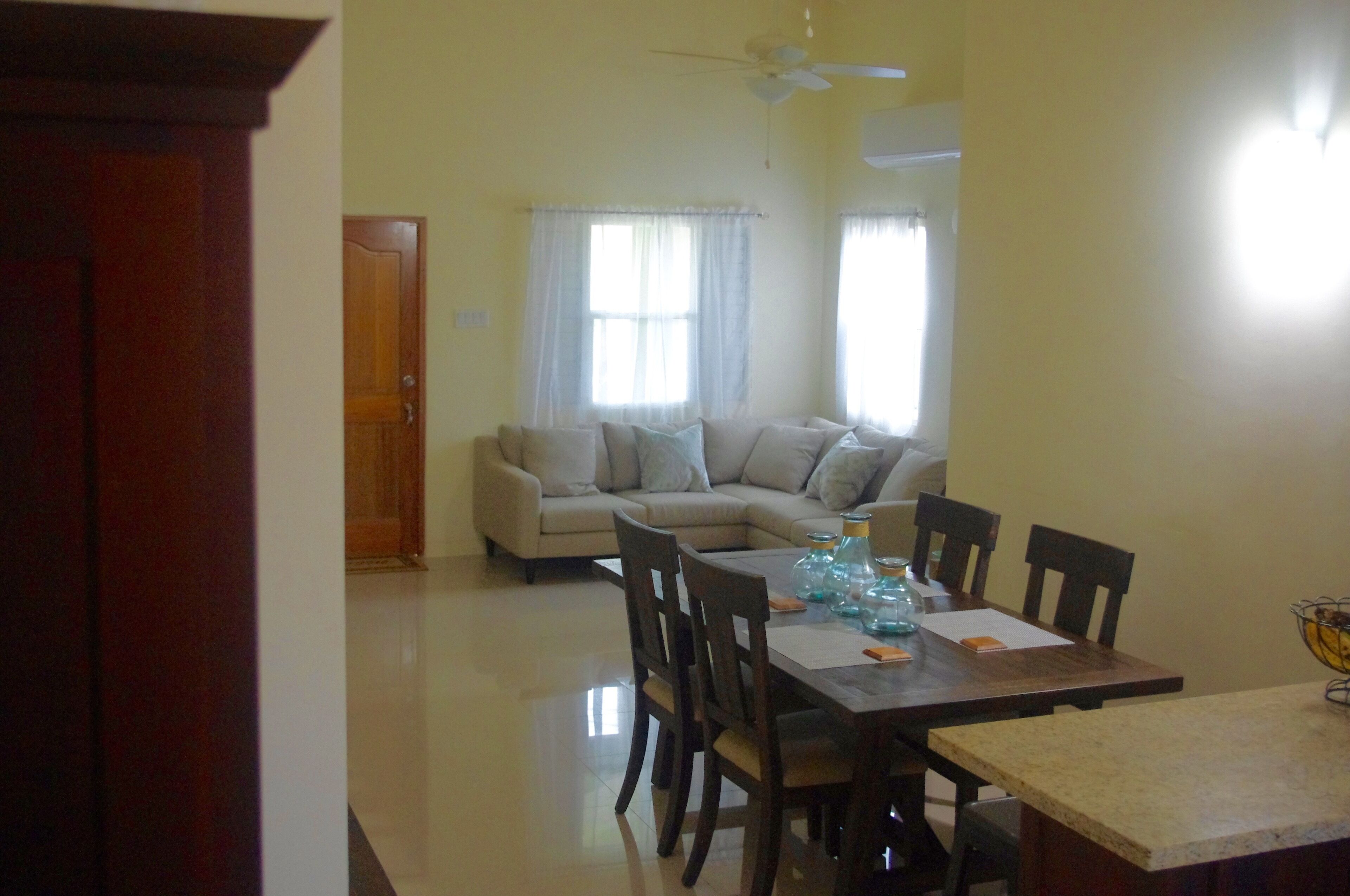 A dining area with a wooden table and chairs, a sofa in the background, and a ceiling fan.