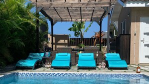 Una piscina con agua cristalina azul, rodeada de sillas de descanso y una pérgola.