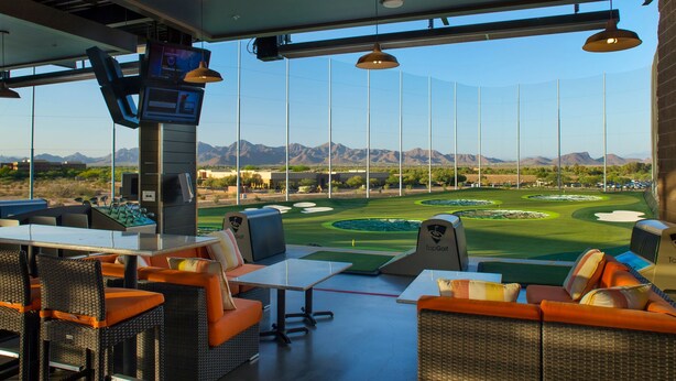 A modern indoor golf facility with seating areas, a large screen, and a view of a golf course. - Ultra-Clean, Designer Condo. Walk to grocery, restaurants, coffee, and shopping! (Scottsdale)