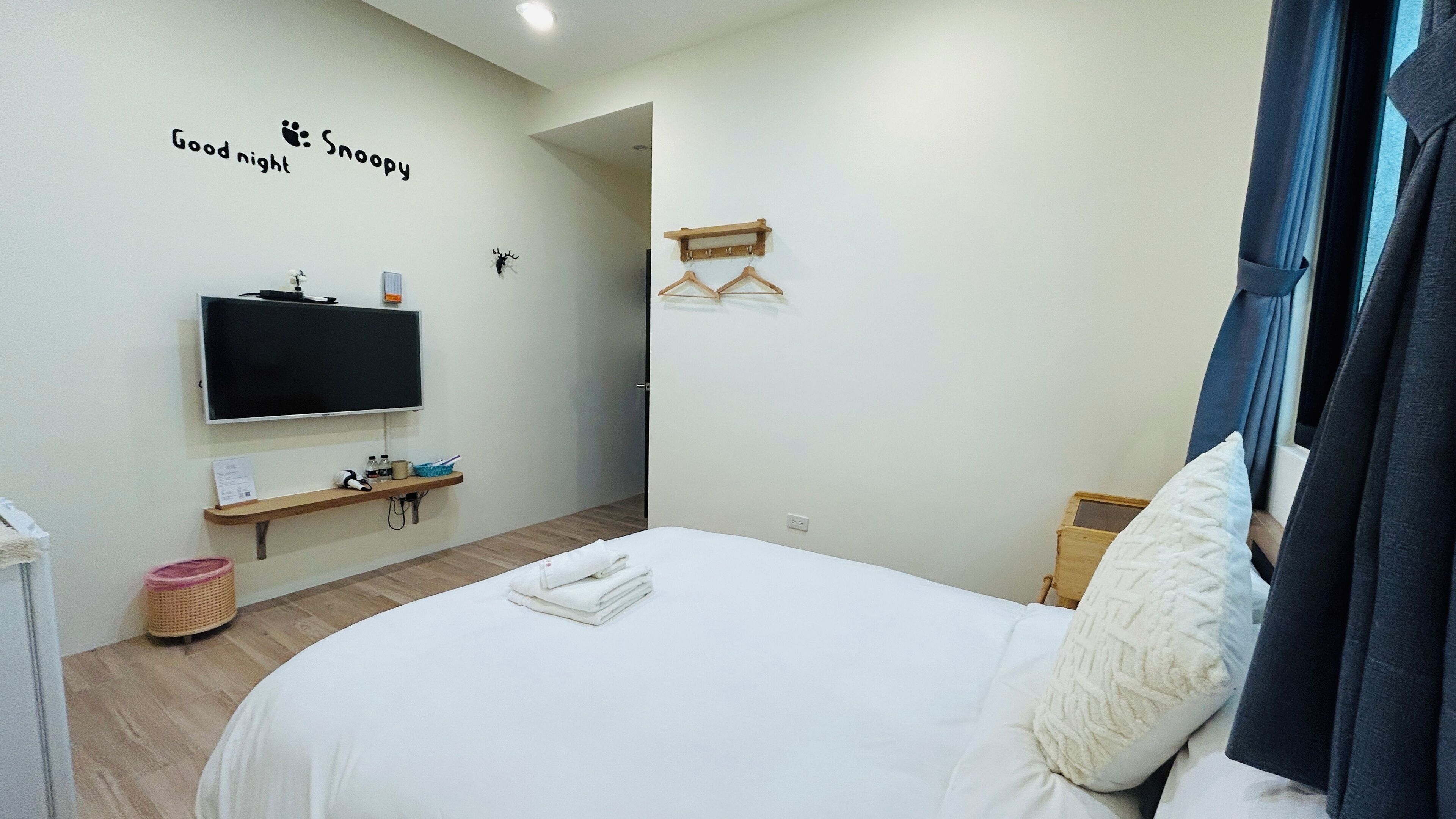 Habitación de hotel con una cama, un televisor montado en la pared, un estante con artículos de tocador y un cartel que dice "Good night Snoopy".