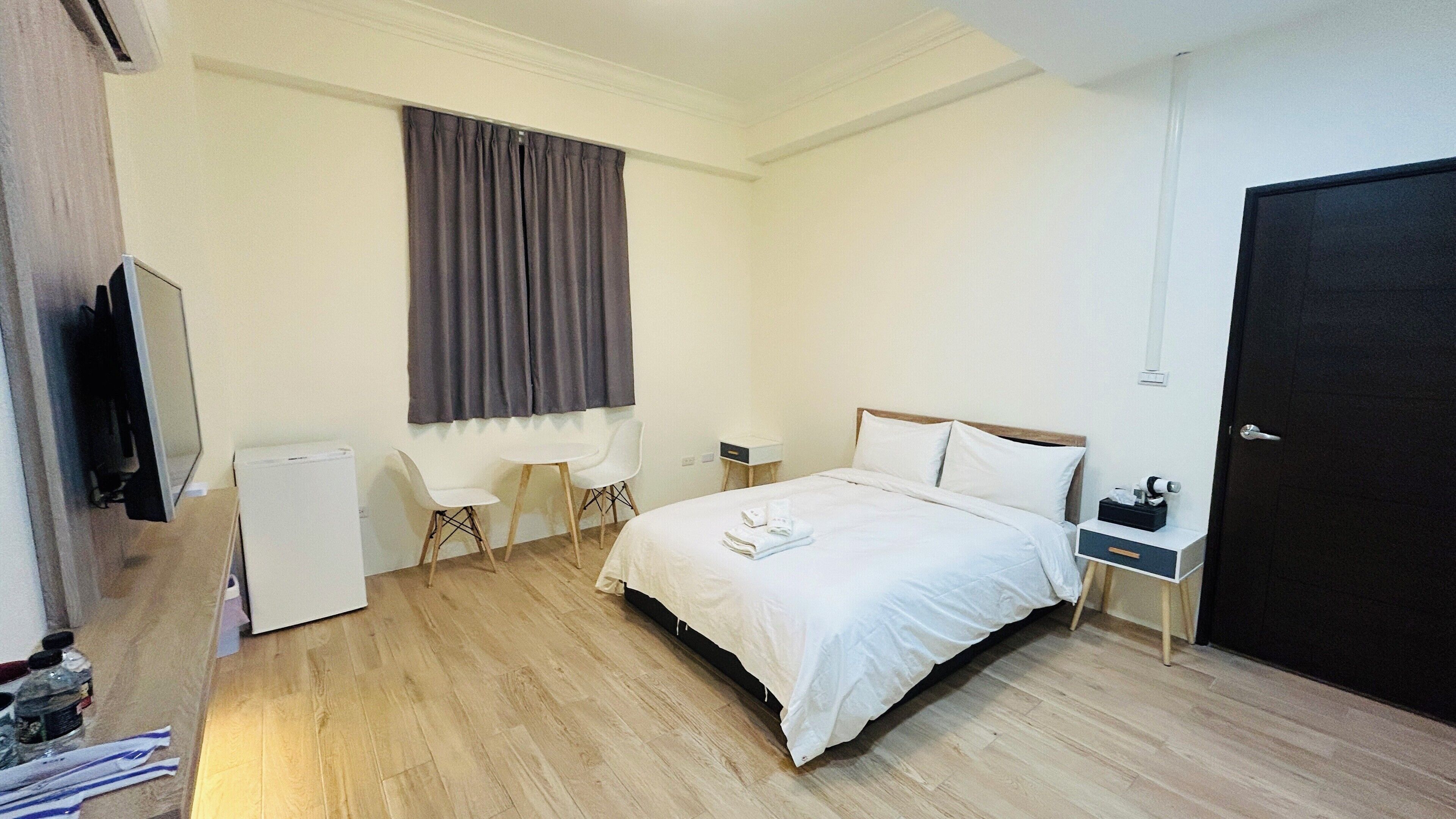 A hotel room with a bed, a desk, a chair, a TV, and a wardrobe.