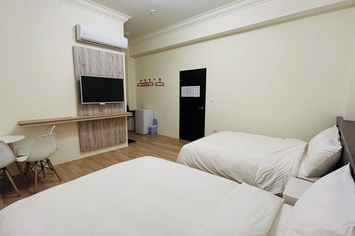 Une chambre d’hôtel avec deux lits, un téléviseur fixé au mur, un petit bureau avec une chaise et une porte sur laquelle est affiché un avis.