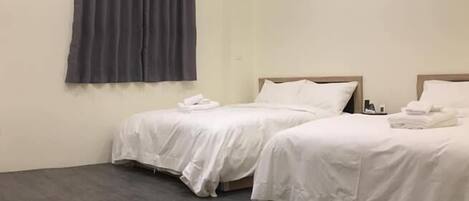 A hotel room with two beds, a large window with curtains, and a wooden floor.