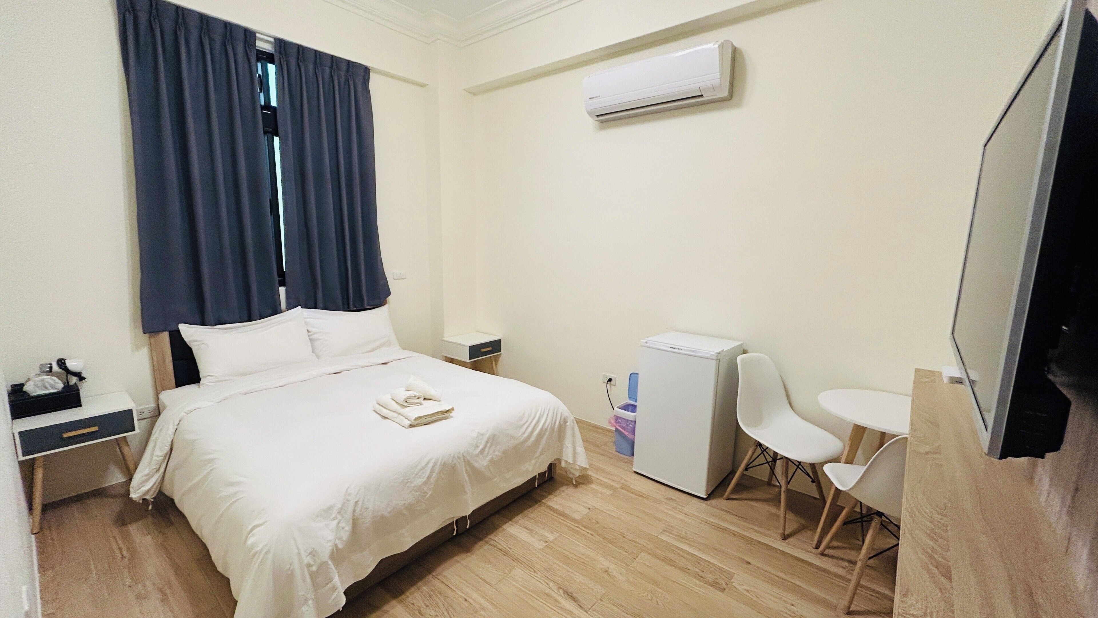 Habitación de hotel con cama, escritorio, silla, refrigerador pequeño y aire acondicionado.