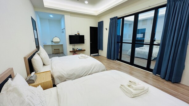 A hotel room with two beds, a TV, a desk, a mirror, and a large window with curtains. - Colorful Guesthouse (Magong)