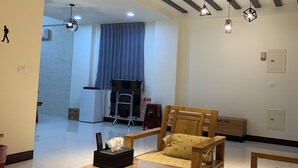 A spacious living room with a wooden dining table, a sofa, and a bench. There are ceiling lights and a wall-mounted shelf. - Colorful Guesthouse (Magong)