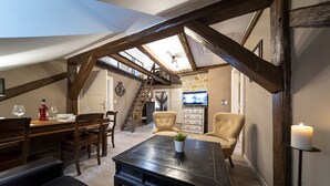 A cozy loft-style room with exposed wooden beams, a dining area with a wooden table and chairs, a comfortable seating area with two armchairs, and a stone fireplace. - OLD TOWN -2 BEDROOM 2 BATHROOM max 8 pers (Prague 1)