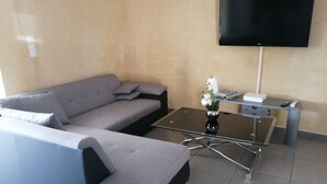 A modern living room with a grey sofa, a glass coffee table, and a flat-screen TV mounted on the wall. - The barn corner of paradise (Leychert)