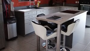 A modern kitchen with a central island, white bar stools, and a stainless steel sink. - The barn corner of paradise (Leychert)