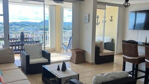 A spacious living room with a sofa, chairs, a coffee table, and a TV. There is a balcony with a view of the city and mountains. - The best vacation in Puerto Rico (Fajardo)