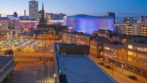 A cityscape at dusk with illuminated buildings, including a distinctive dome-shaped structure with blue lighting. - Tudors eSuites Birmingham Apartments Jewellery Quarter (Birmingham)