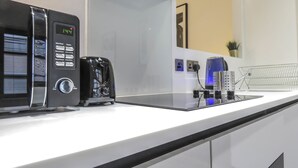 A modern kitchen with a coffee maker, a digital clock, and a power strip. - Tudors eSuites Birmingham Apartments Jewellery Quarter (Birmingham)
