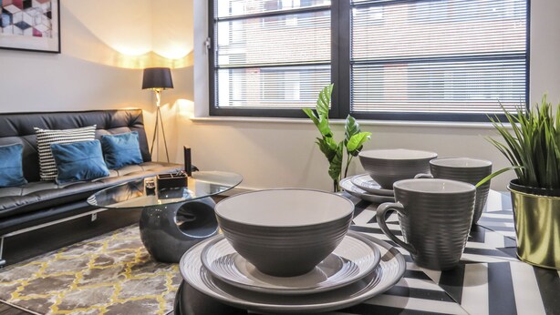 A modern living room with a sofa, coffee table, and dining set. - Tudors eSuites Birmingham Apartments Jewellery Quarter (Birmingham)
