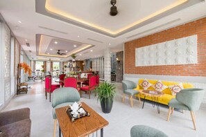 En moderne hotellobby med et spiseområde, et loungeområde med en gul sofa, og en stor mur med dekorative paneler.
