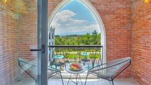Un balcón con vistas a una piscina y follaje, una mesa con fruta y dos sillas.
