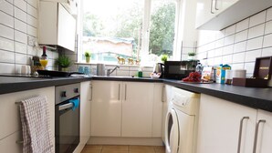 Une cuisine compacte avec des meubles blancs, un lave-linge et une fenêtre donnant sur un espace verdoyant.
