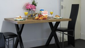 Une table de petit-déjeuner avec des croissants, une boîte de Nutella, du jus de fruits et un vase rempli de fleurs.
