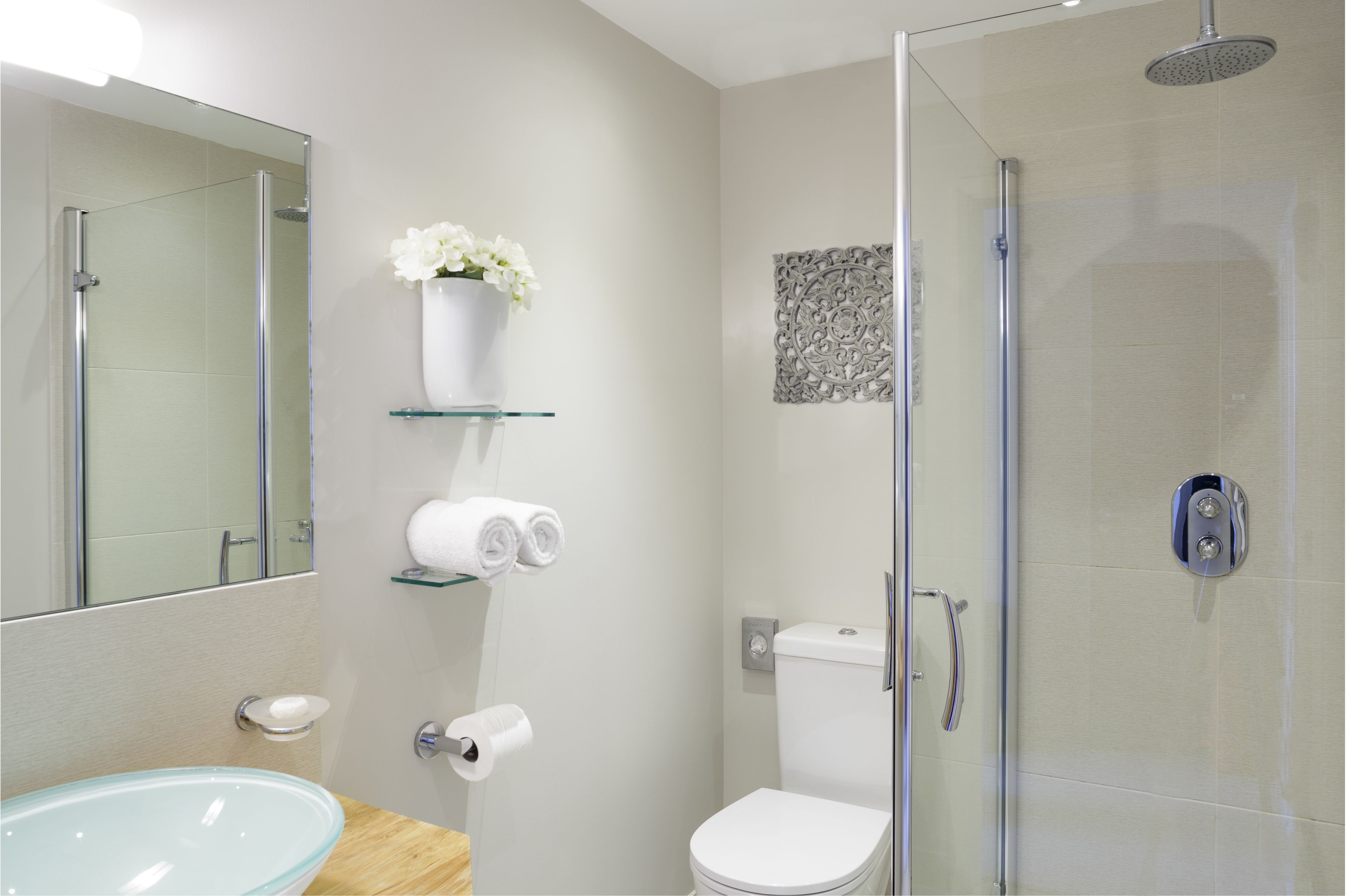 A modern bathroom with a glass shower enclosure, a glass sink, and a toilet.