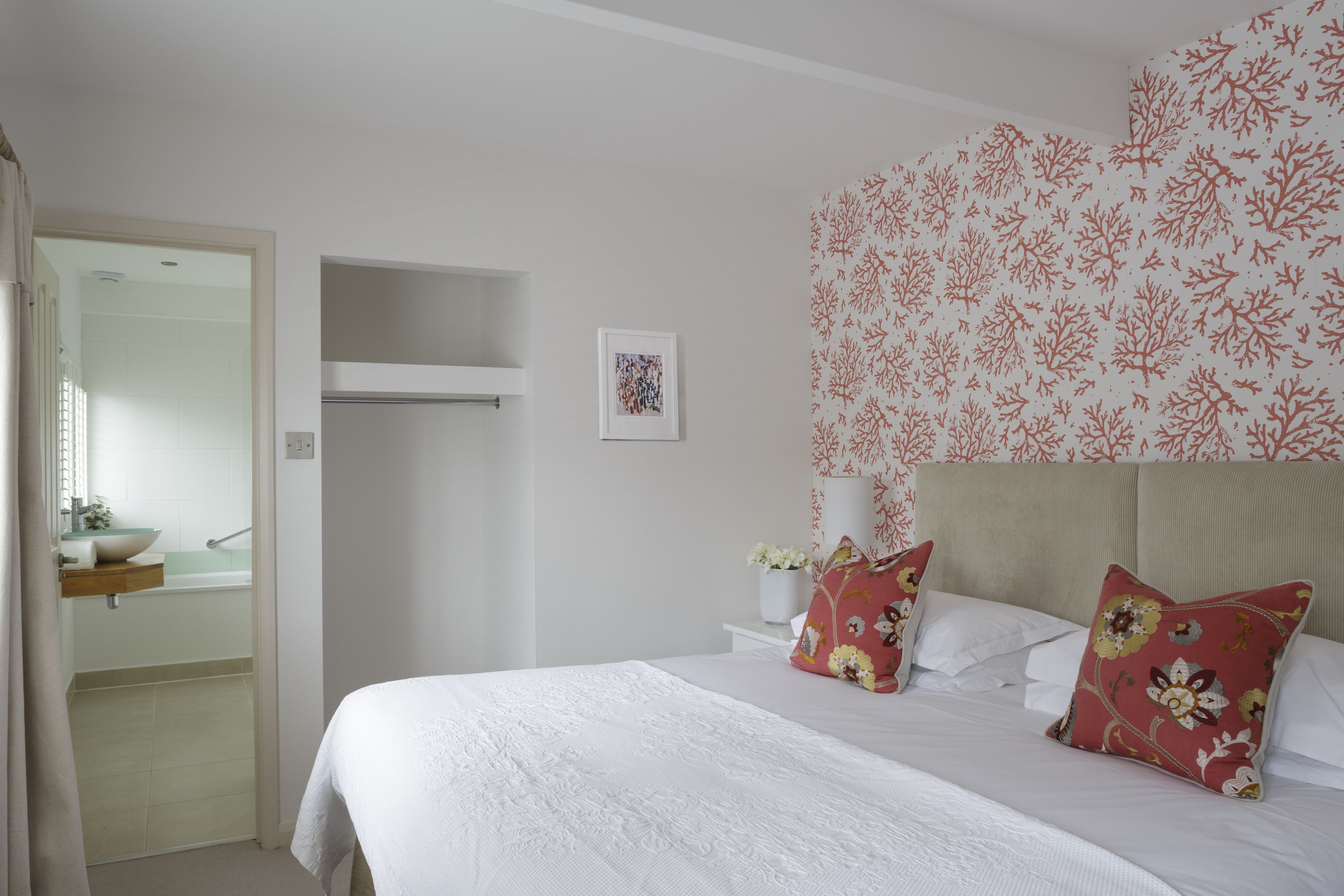 A bedroom with a bed, pillows, a nightstand, a wall-mounted shelf, and a framed picture.