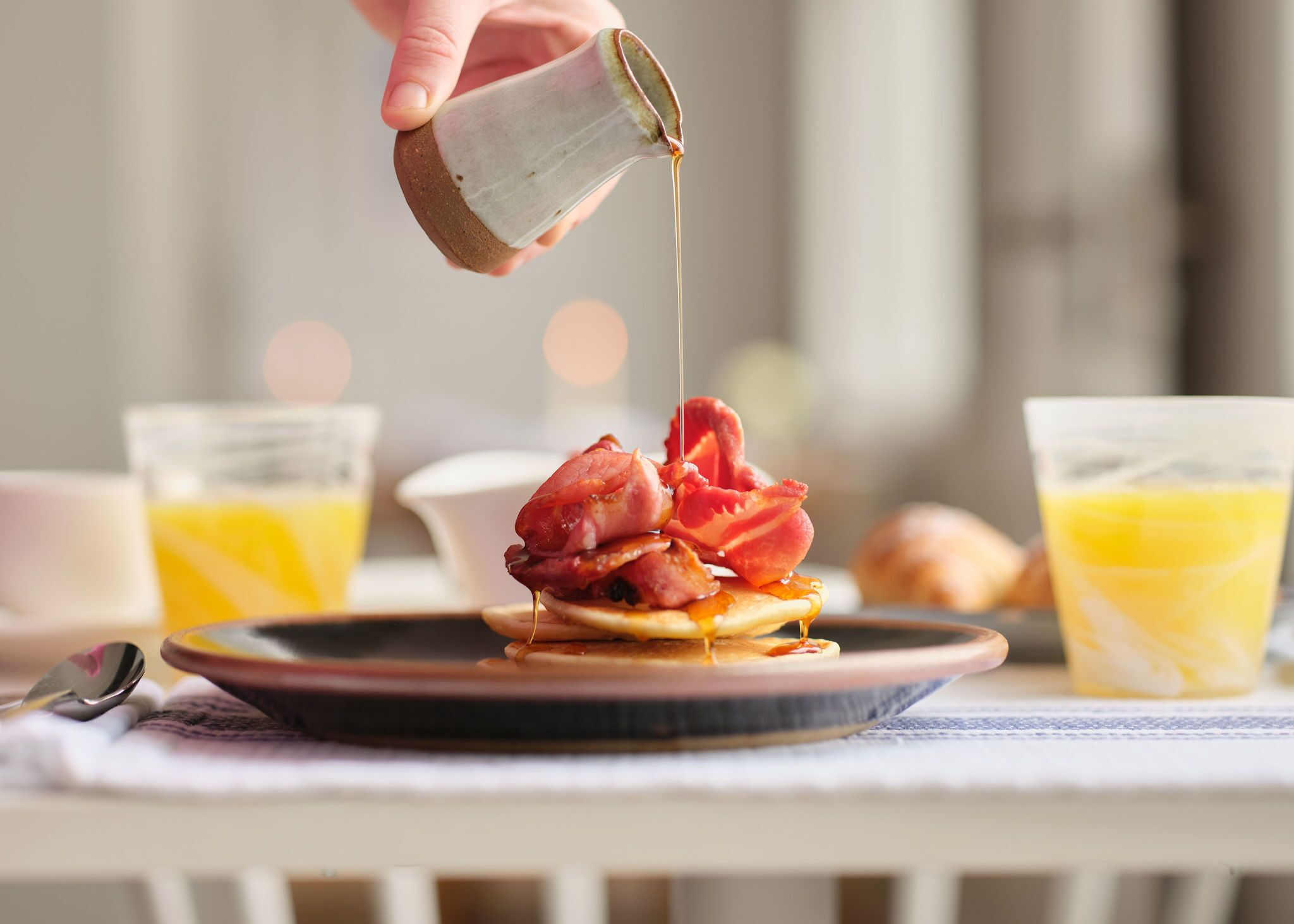 A breakfast plate with bacon, pancakes, and syrup being poured.