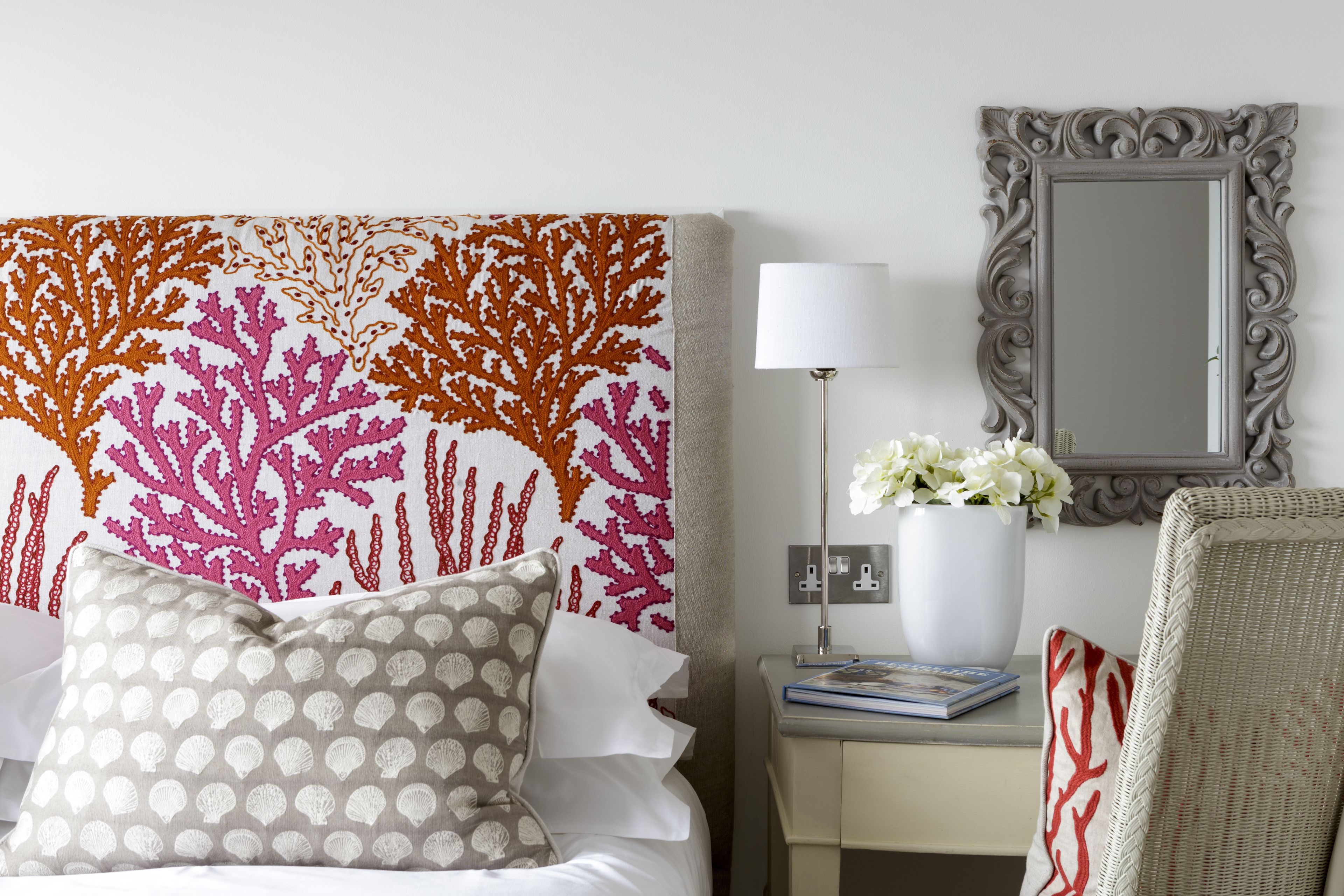 A neatly arranged hotel room with a bed, a nightstand, a lamp, a mirror, and a chair.