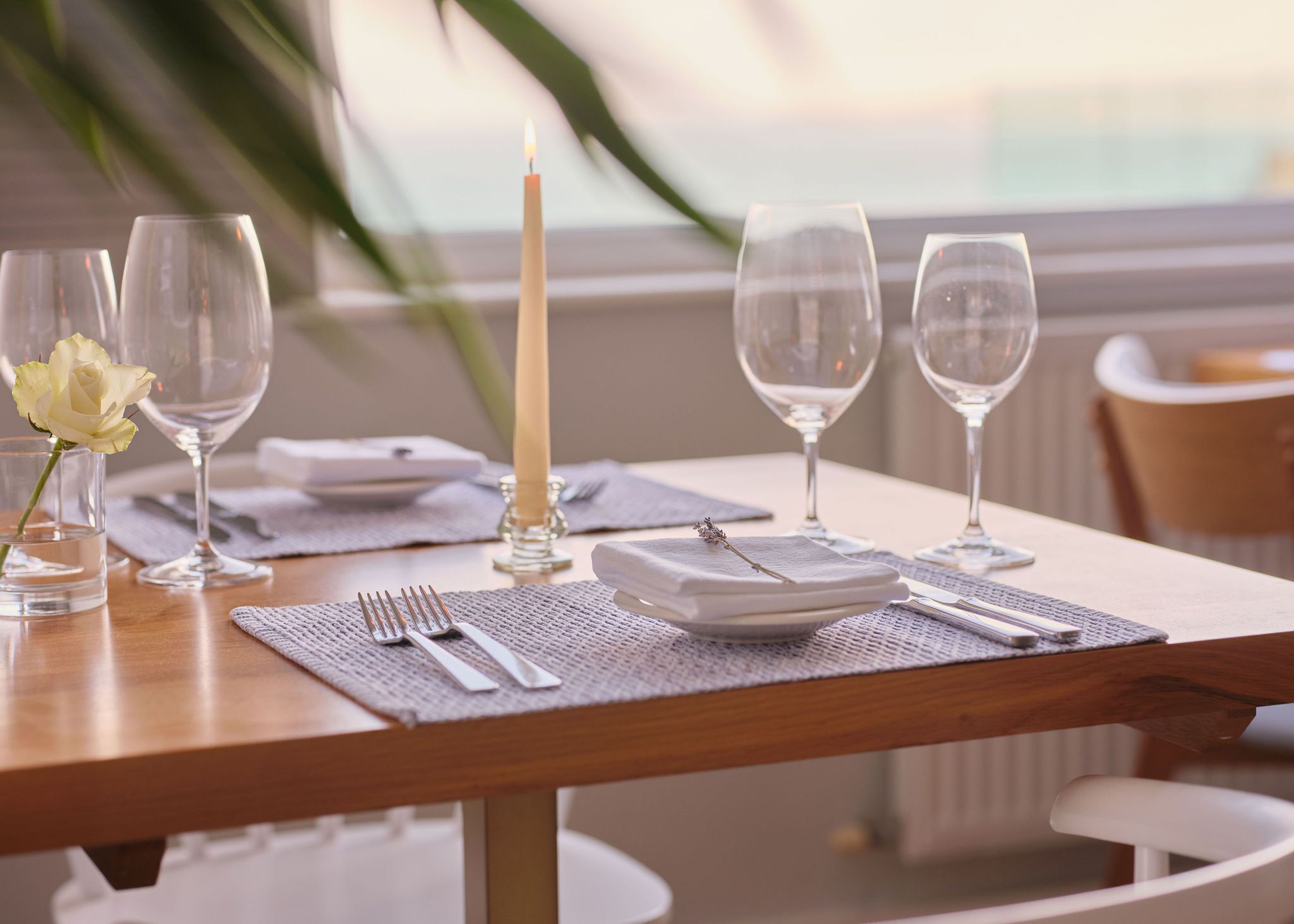 A dining table set with plates, glasses, cutlery, and a candle.