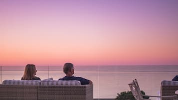 A couple seated on wicker lounge chairs overlooking a body of water during sunset.