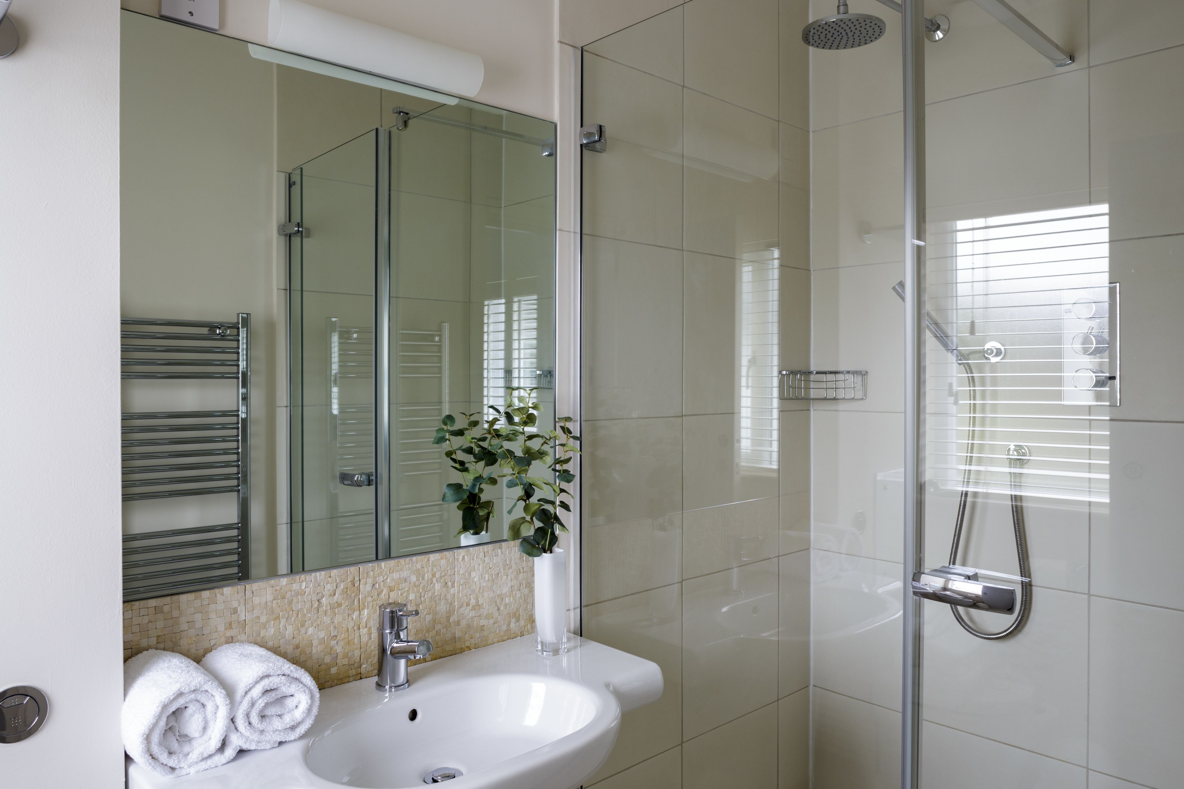 Een moderne badkamer met een douchecabine van glas, een witte wastafel en een spiegel erboven.