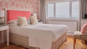Habitación de hotel con una cama grande, una mesita de noche, una silla, un ventanal con vistas y un papel tapiz estampado.