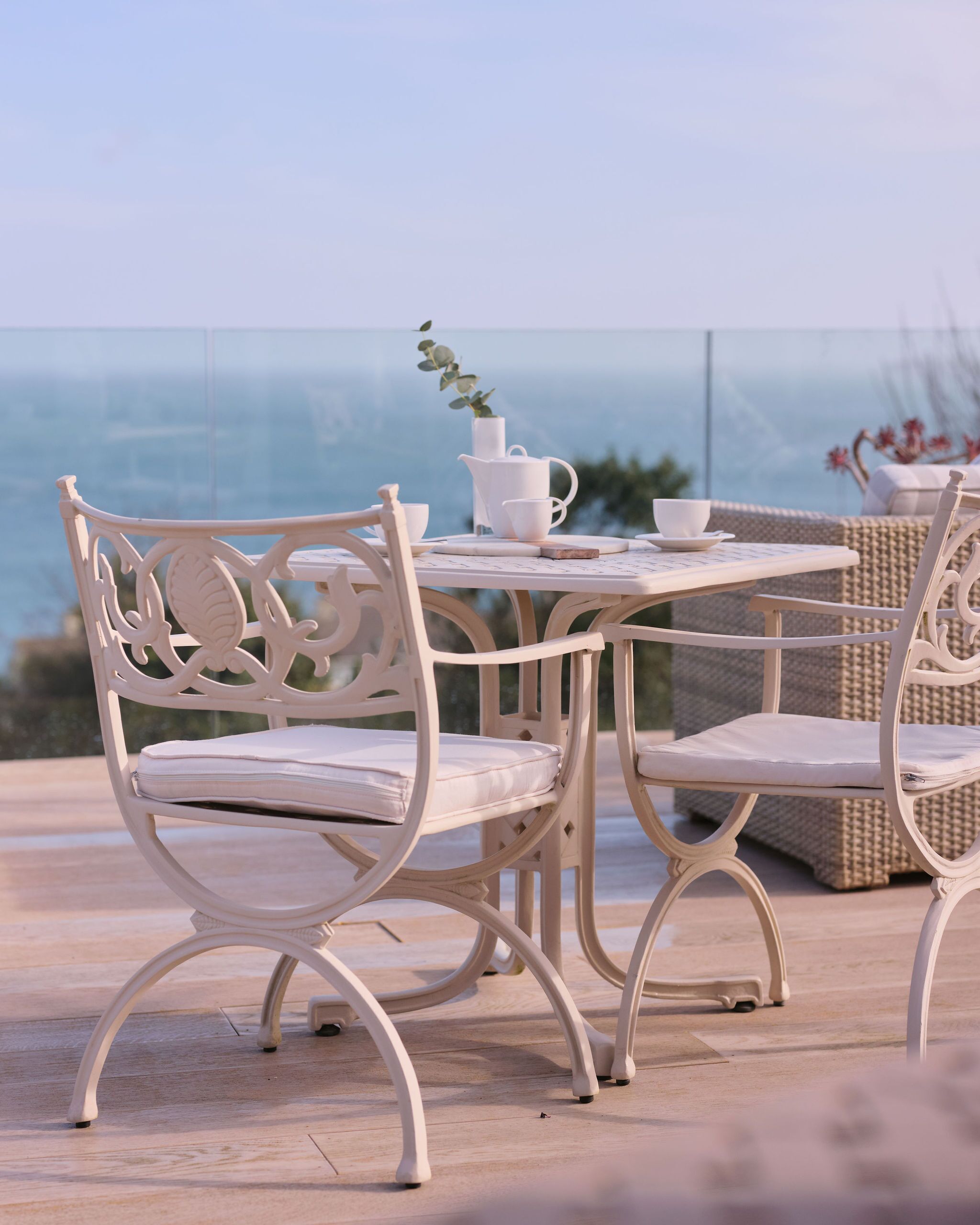 A white outdoor dining set with a view of the ocean.