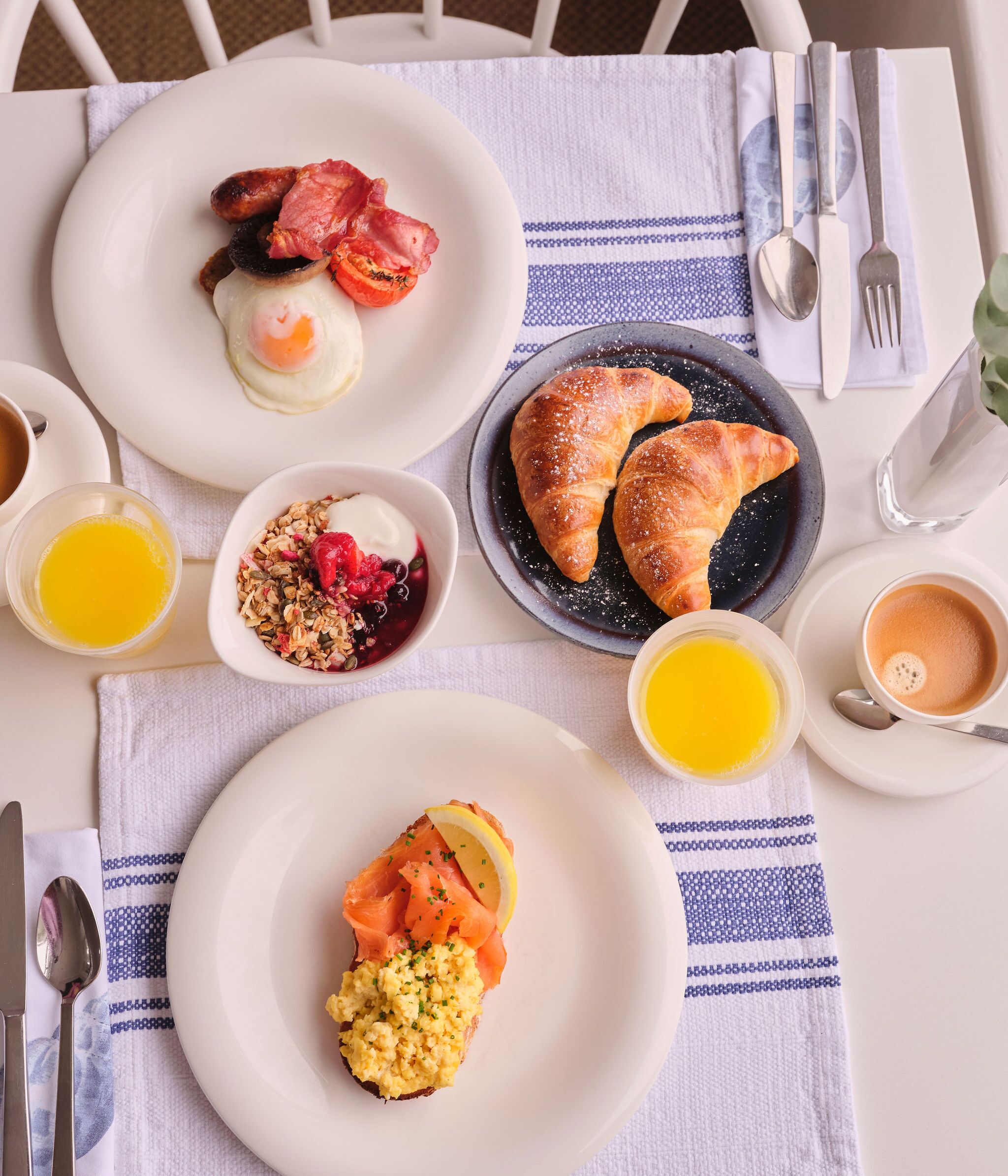 A breakfast setting with plates of eggs, bacon, croissants, and smoked salmon.