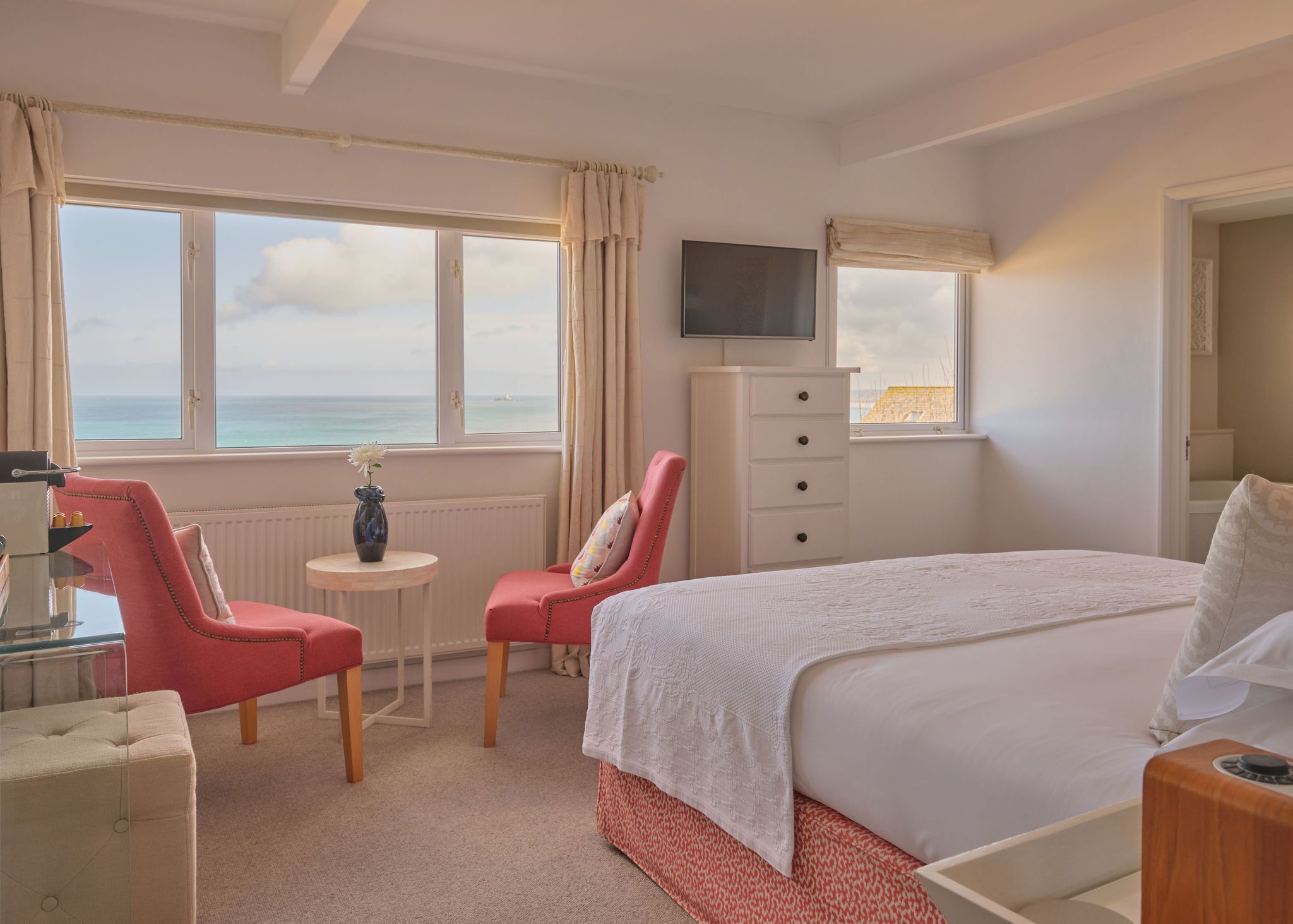 Une chambre d’hôtel avec un lit, deux chaises, une petite table, un téléviseur et une vue sur la mer.