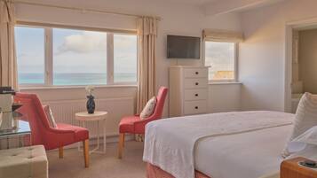 Une chambre d’hôtel avec un lit, deux chaises, une petite table, un téléviseur et une vue sur la mer.