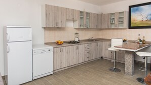 Een moderne keuken met houten kastjes, een ingebouwde vaatwasser, een aanrecht met een fruitschaal, een blender en een barkruk.