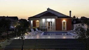Een moderne woning met een zwembad, een overdekt terras en een goed verlichte entree.