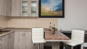 Een moderne keuken met een marmeren aanrecht, twee witte stoelen en een lijstwerk schilderij boven de gootsteen.