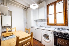 Una cocina compacta con armarios blancos, una mesa de comedor de madera, una lavadora y un horno.