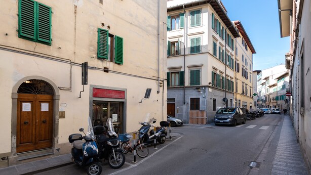 Una calle estrecha flanqueada por edificios históricos, scooters aparcados y automóviles.