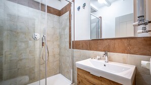 Un baño moderno con cabina de ducha de vidrio, tocador de madera con lavabo blanco y un espejo grande.